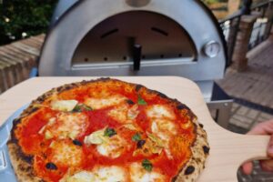 Versgebakken pizza op houten pizzaschep voor Clementino gasoven