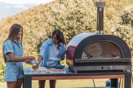 Dames die pizza beleggen naast Clementi GOLD gas pizzaoven met rode kap