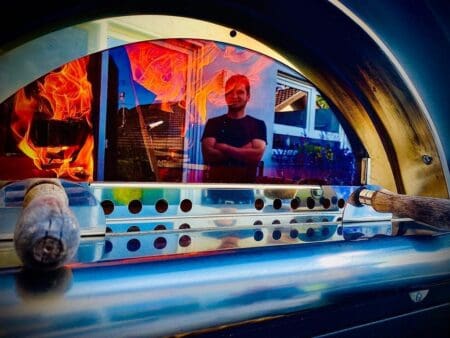 Kok staat te kijken naar brandende pizzaoven door glazen venster