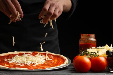 chef strooit kaas op pizza tijdens bereiding